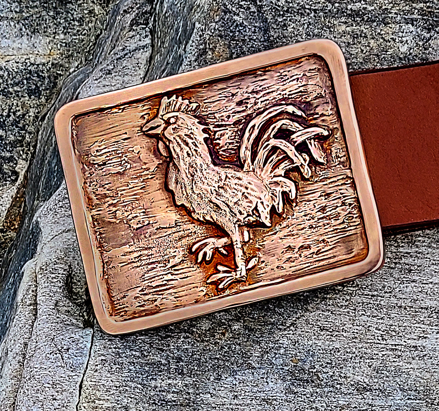 Rooster Buckle and belt shown with a stone background.
